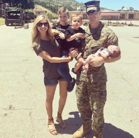 Wife holds son next to army husband who is holding their two other children