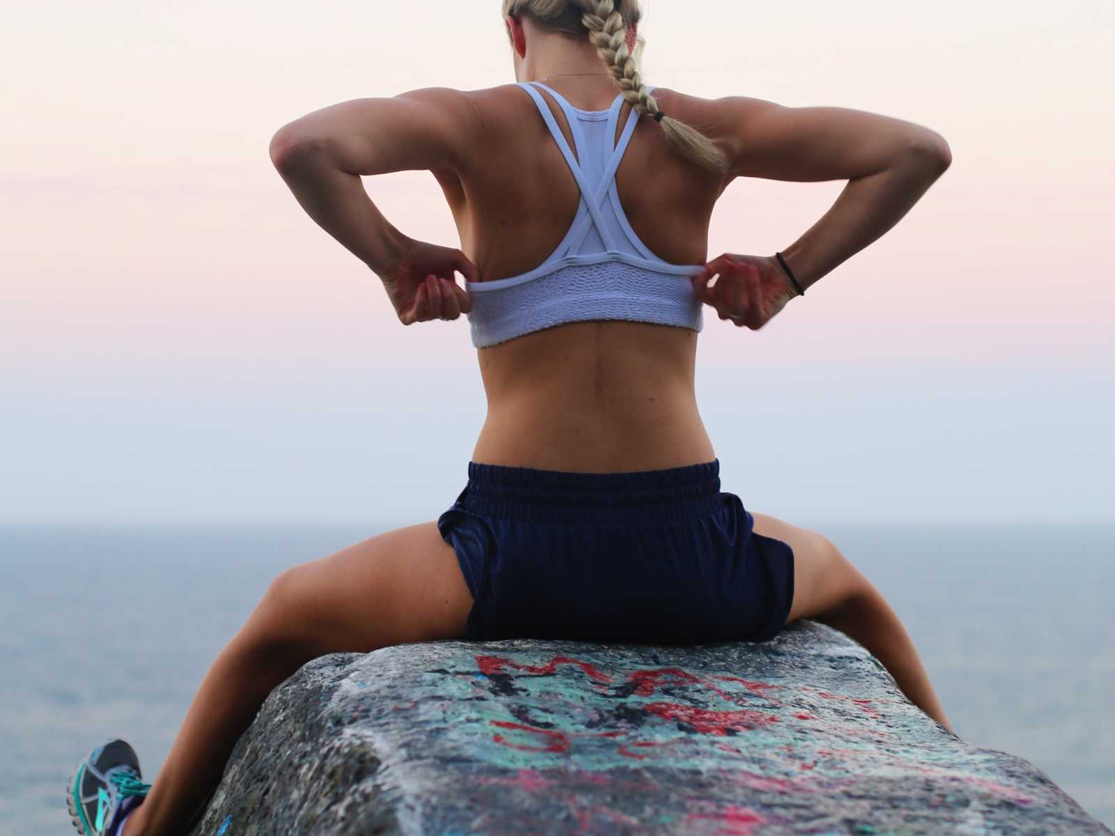 View of back of paraplegic woman straddling rock adjusting her sports bra with scar peaking thorugh