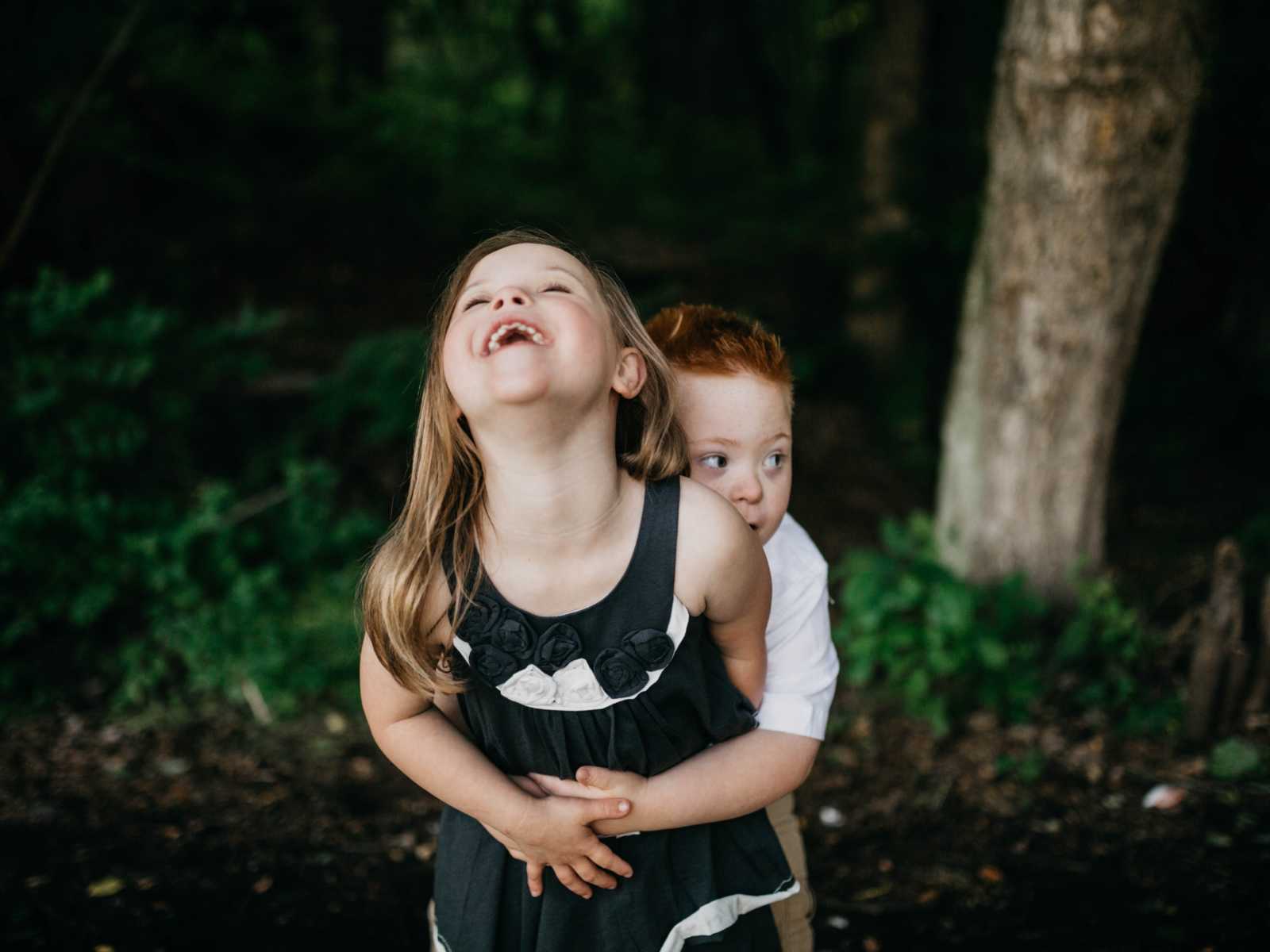 Down syndrome girl laughing with down syndrome boy wraps his arms around her