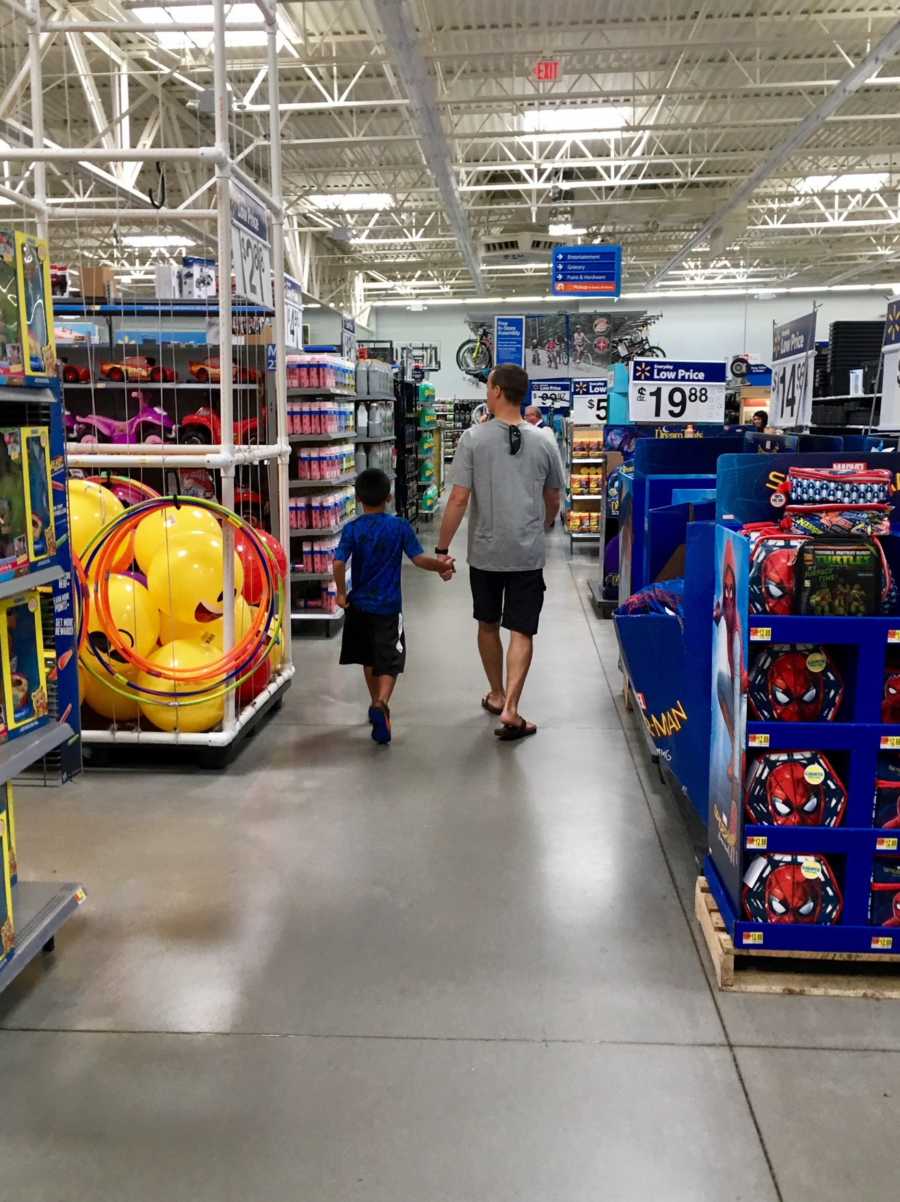 Father holding hand with adopted son walking down aisle of toy store