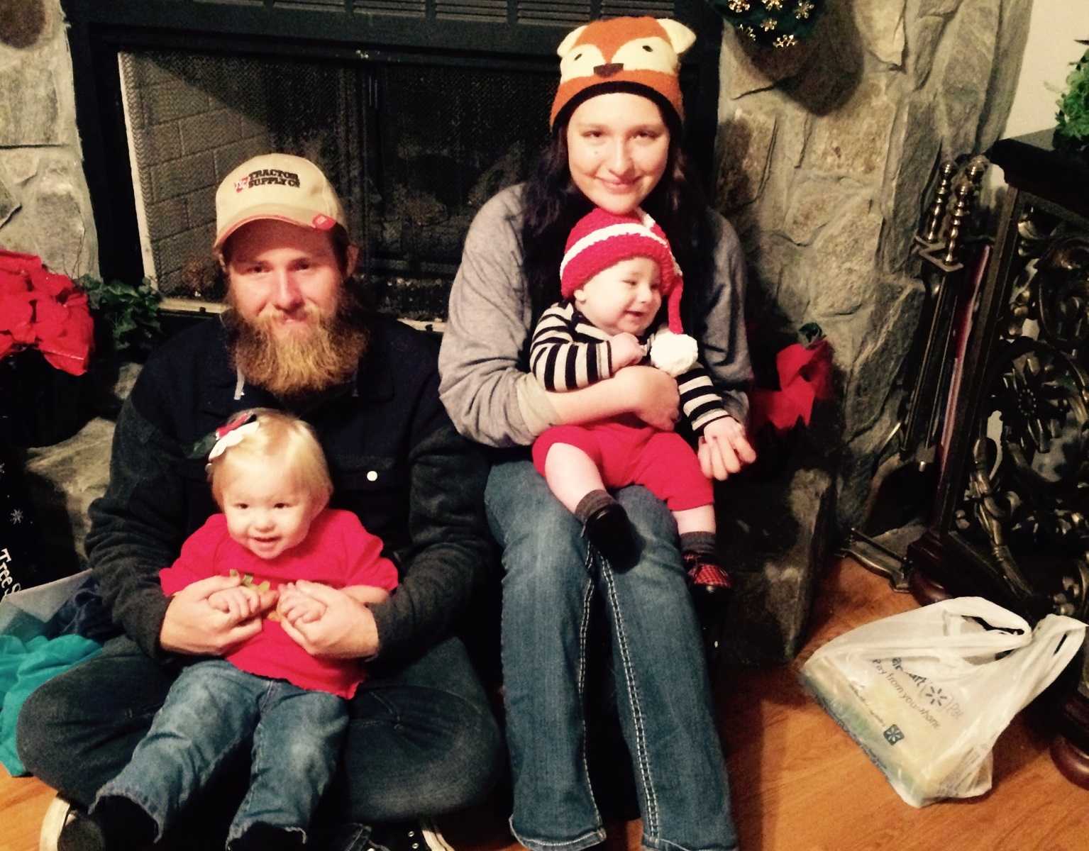 Mother with diabetes leans on fireplace with baby in her lap next to husband with daughter in his lap