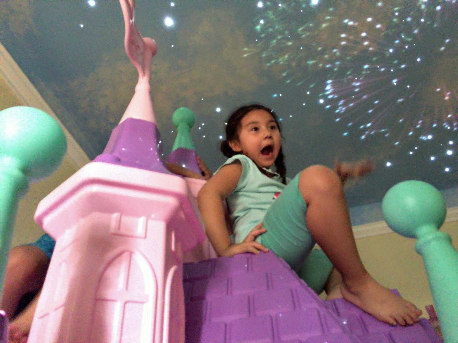 Little girl sits on top of princess castle in her bedroom and ceiling has fireworks