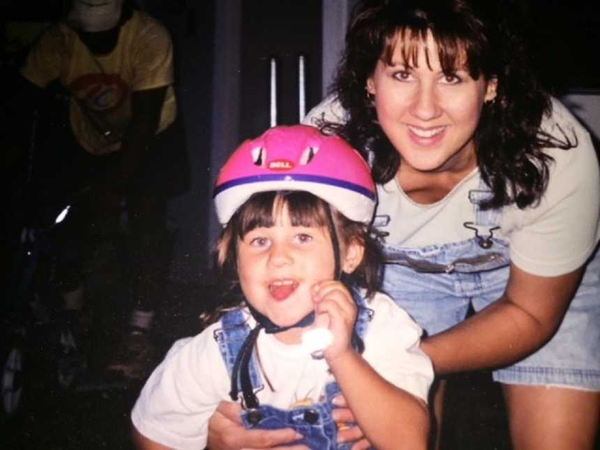 Mother who later is diagnosed with cancer holds on to daughter who makes silly face wearing pink and purple helmet