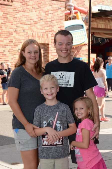 Husband and wife stand smiling with birth son and daughter before adopting