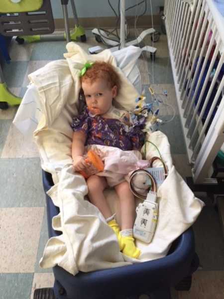 Toddler sits in cart in hospital waiting to have open heart surgery