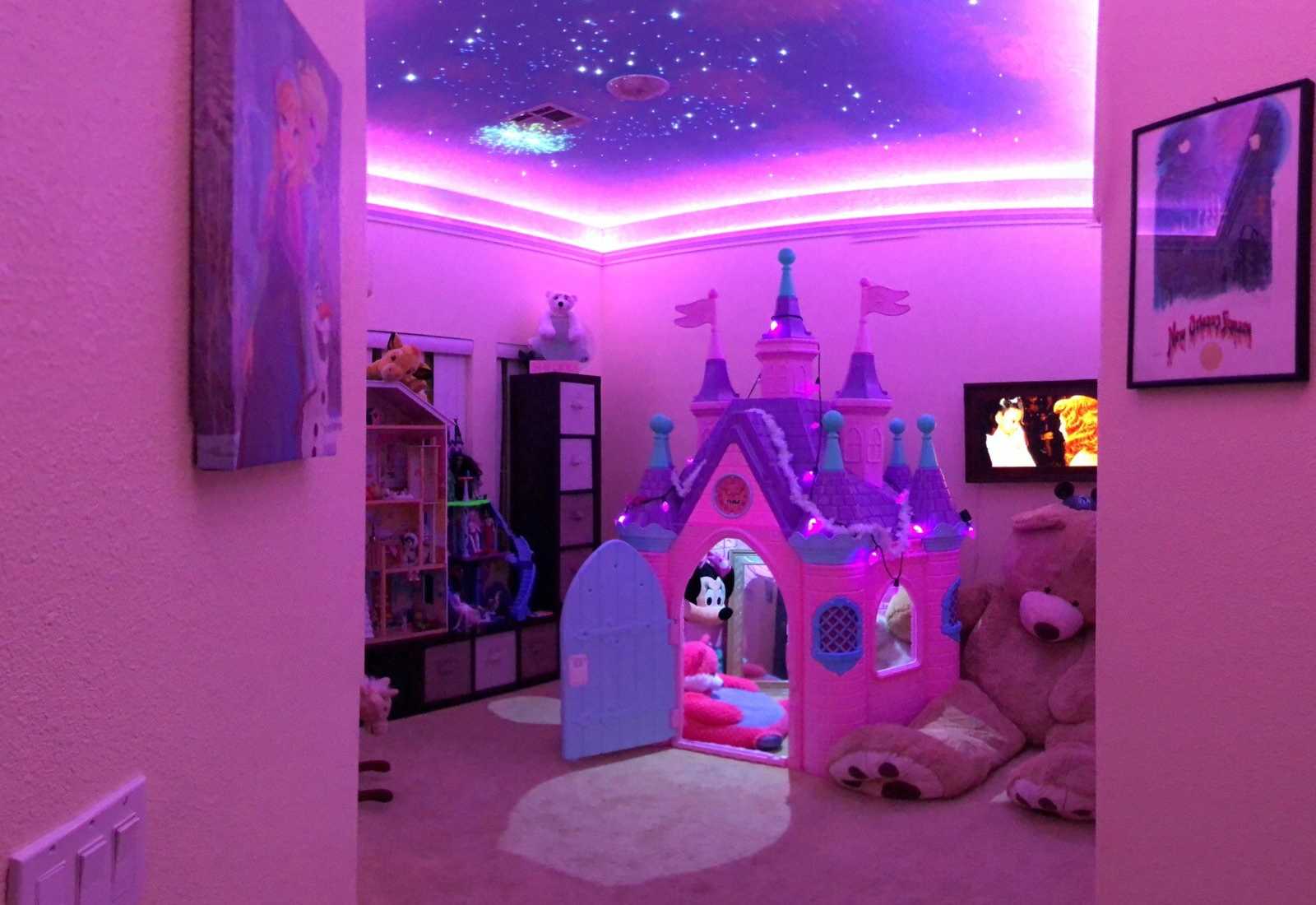 Little girl's Disney inspired room lit up in pink with pink castle in center of room
