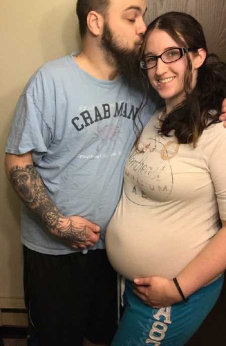 Sober woman holds pregnant stomach while husband kisses her forehead 
