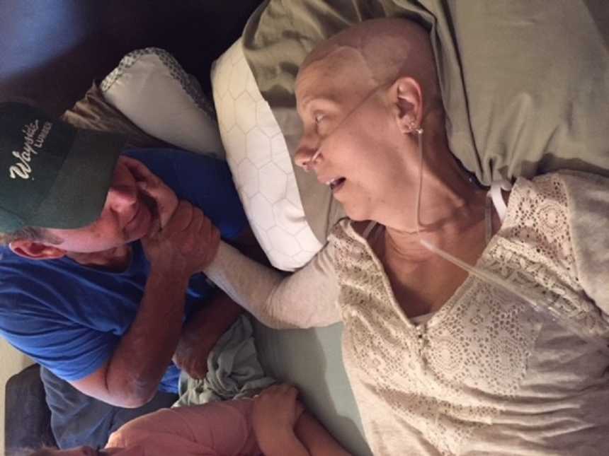 Cancerous mother lays in bed next to husband with her hand on his cheek