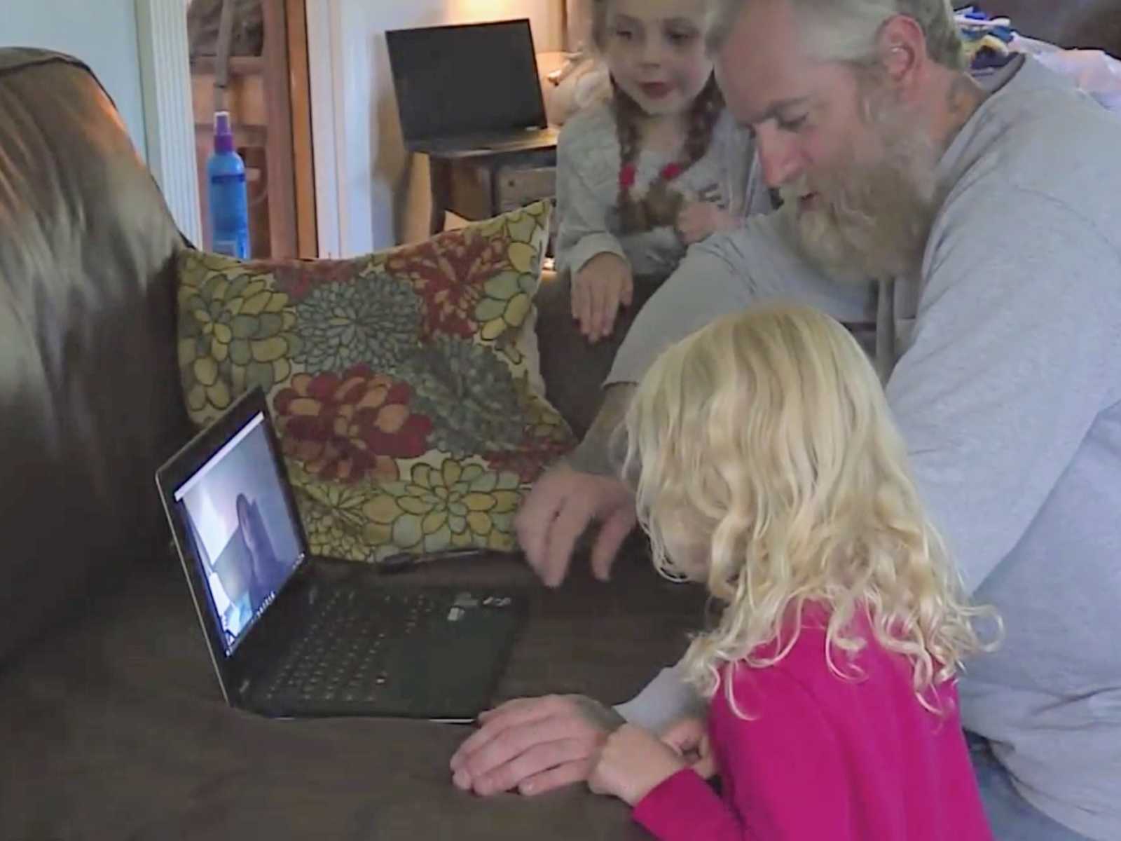 Father watching video on computer with two daughters of his late wife and their mother