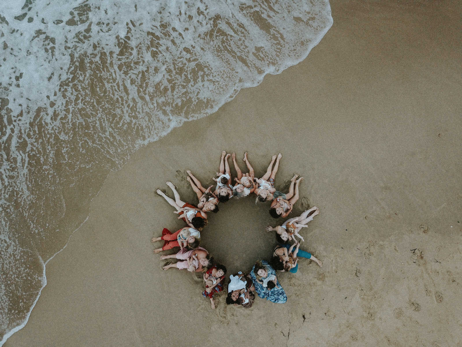 Aerial view of women sitting in a circle on the beach with their babies in their laps