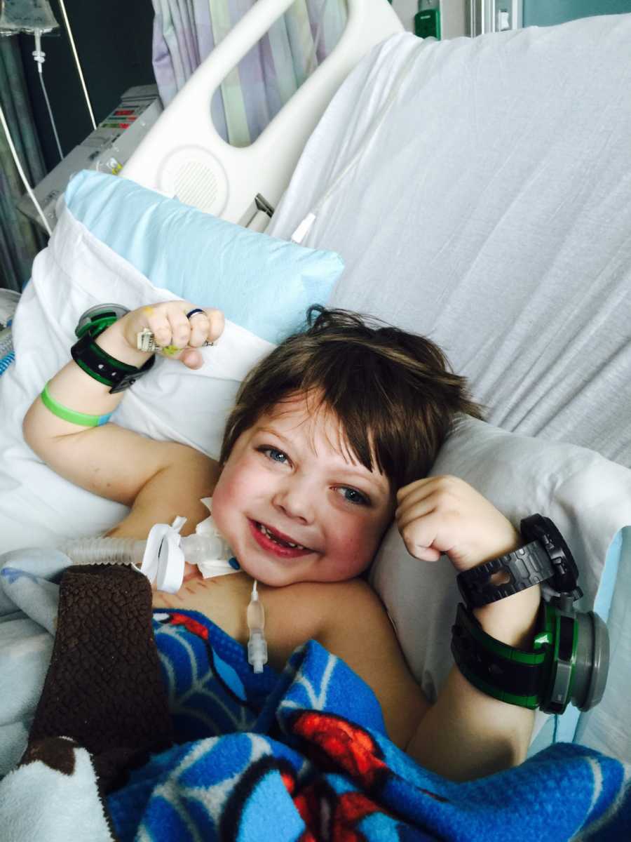 Young boy smiling and flexing his muscles in hospital bed recovering from life threatening strep throat