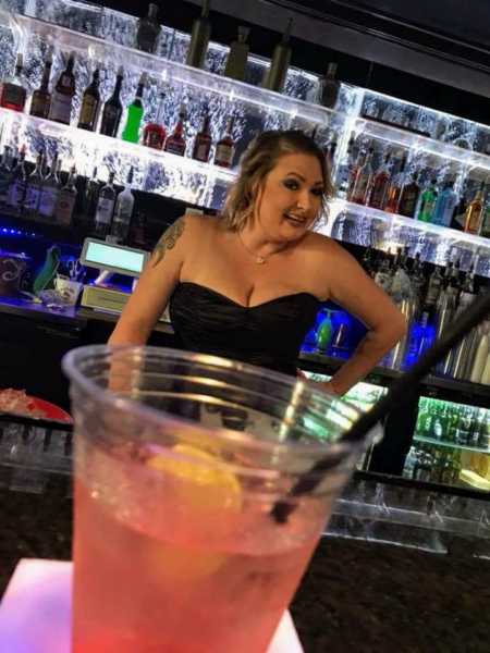 Lesbian woman standing in front of bar with hand on her hip
