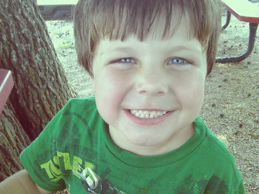 Young boy who had life threatening strep throat sits at picnic table smiling