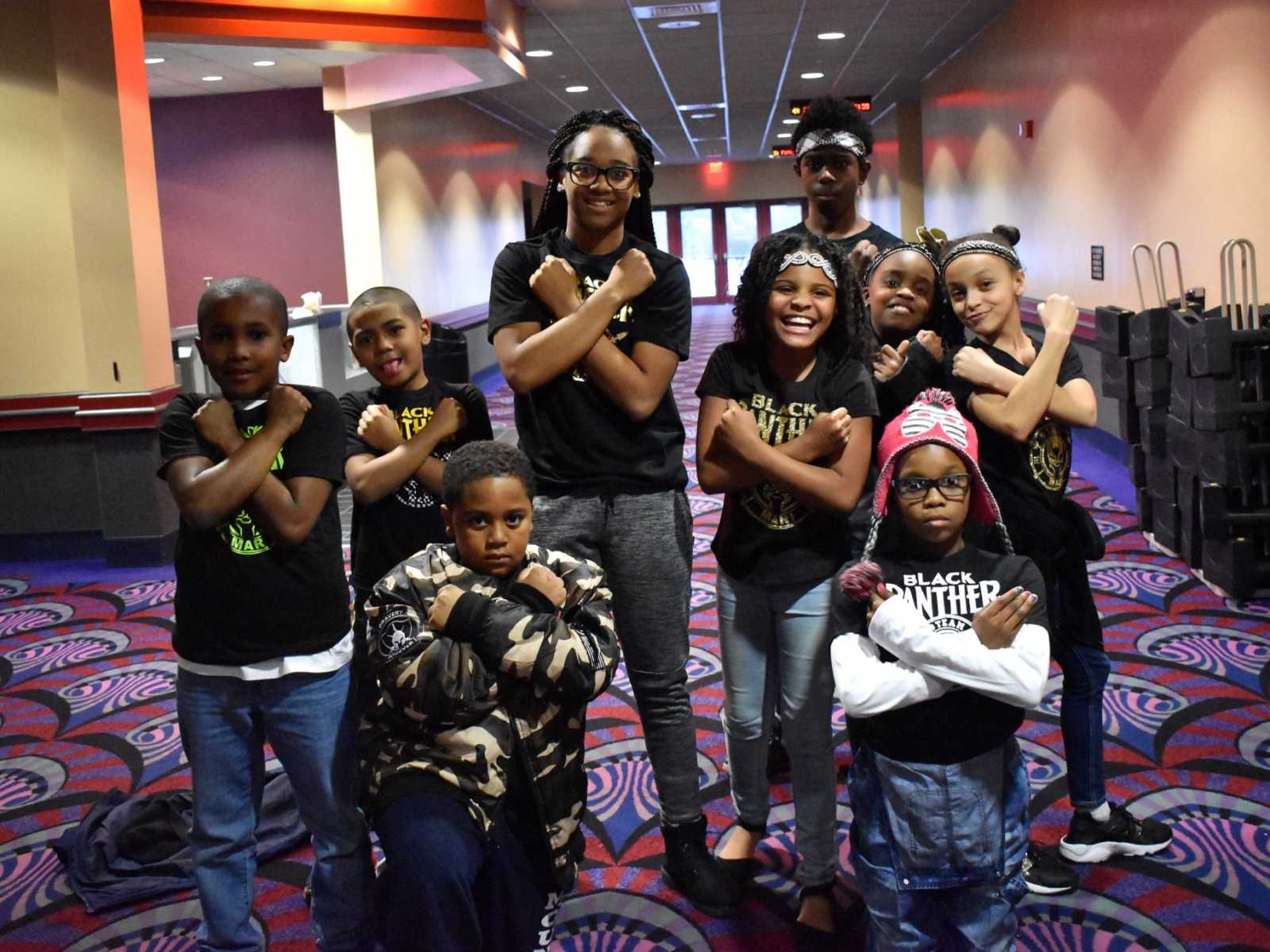 Teens and young kids from Flint, Michigan stand in movie theater hallway with arms crossed in front of chest