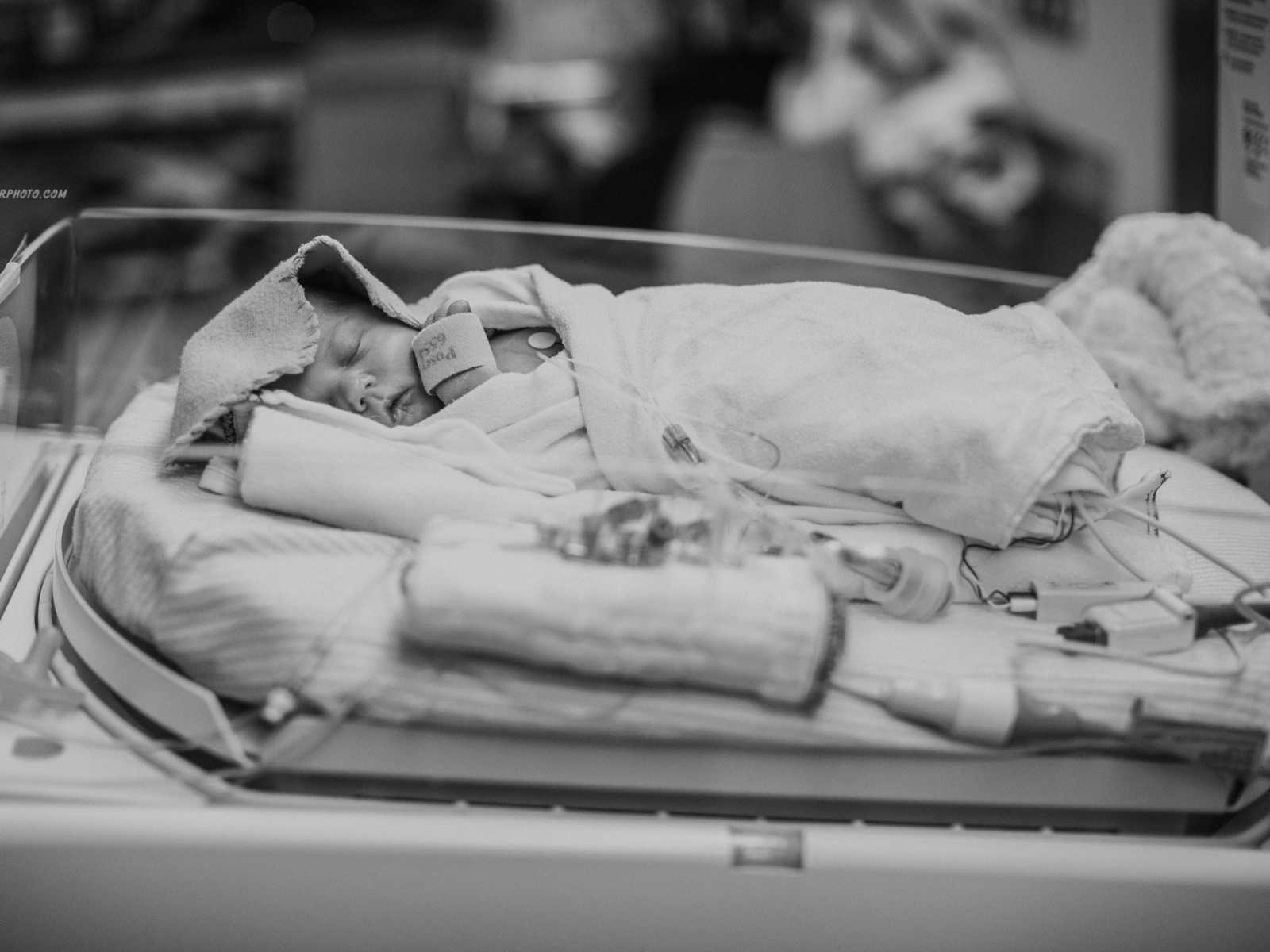 Newborn sleeping in hospital bed completely wrapped in blankets so only his face shows