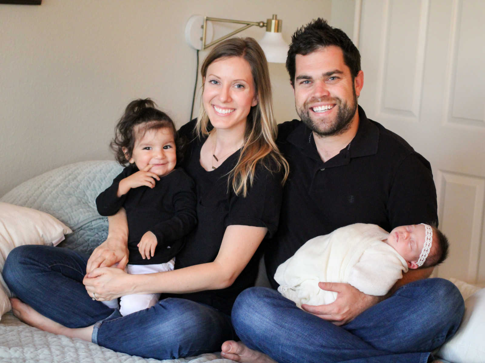 Mother holds adopted daughter in lap next to husband who is holding newborn daughter