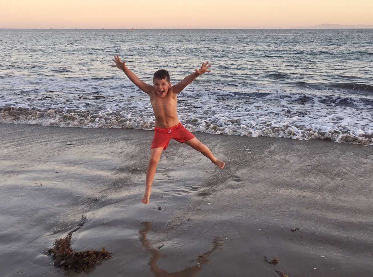 Boy in swimsuit jumps in air on ocean shore