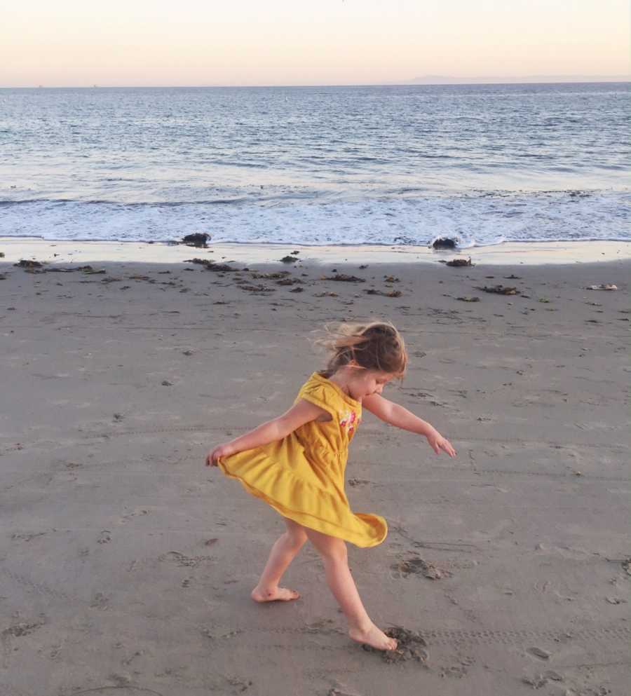 Little girl in yellow dress twirling in sand in front of ocean 