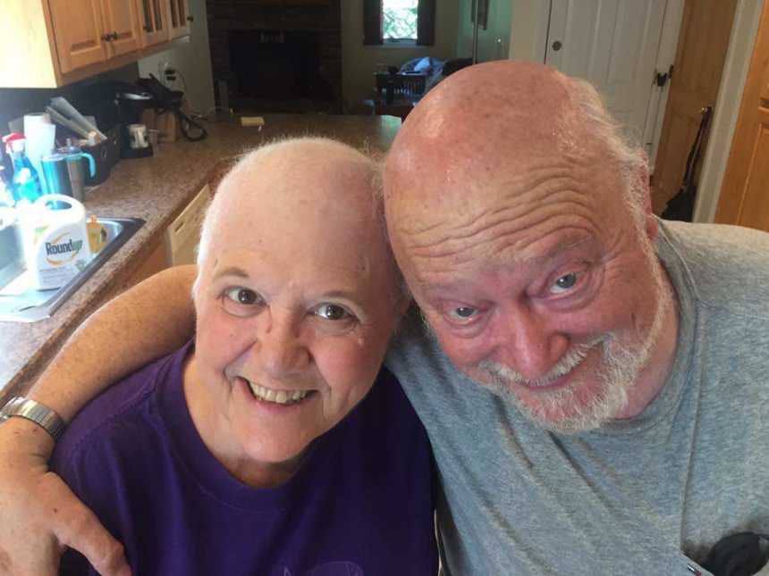 Woman with small cell cancer who lost her hair smiles with husband for selfie in kitchen