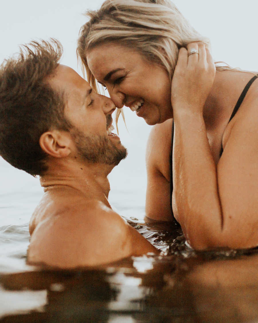 "Curvy" woman and husband nose to nose smiling in ocean