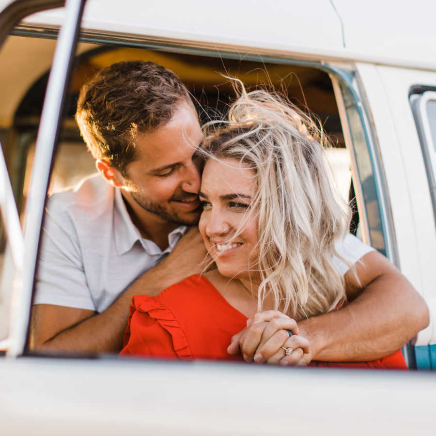 "Curvy" wife leans against husband who is sitting in drivers seat of car with arms around her