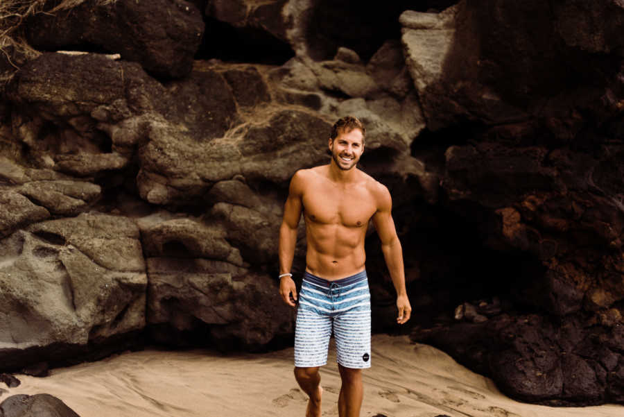 Shirtless man on beach standing in front of large rocks