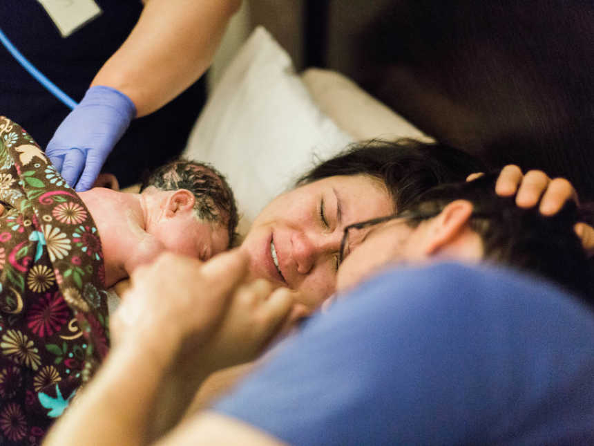 Woman who just gave birth lays in bed with newborn on her chest next to husband