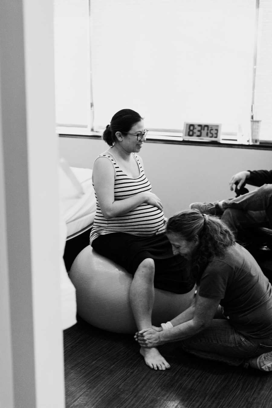 Pregnant woman sits on exercise ball while another woman massages her ankles