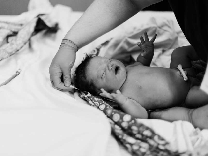 Newborn lies on blanket while nurse tends to her