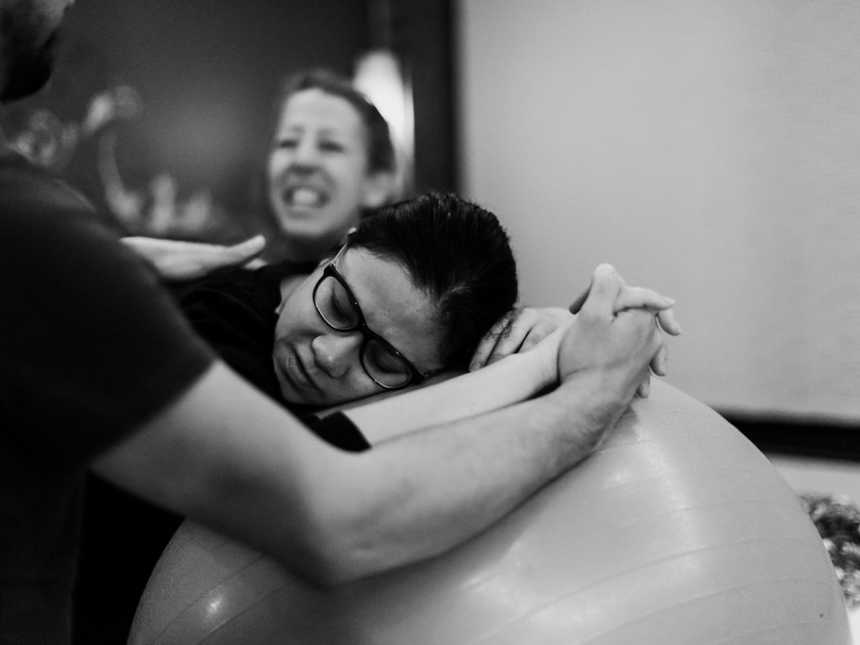 Pregnant woman leans head on medicine ball while holding man's hand