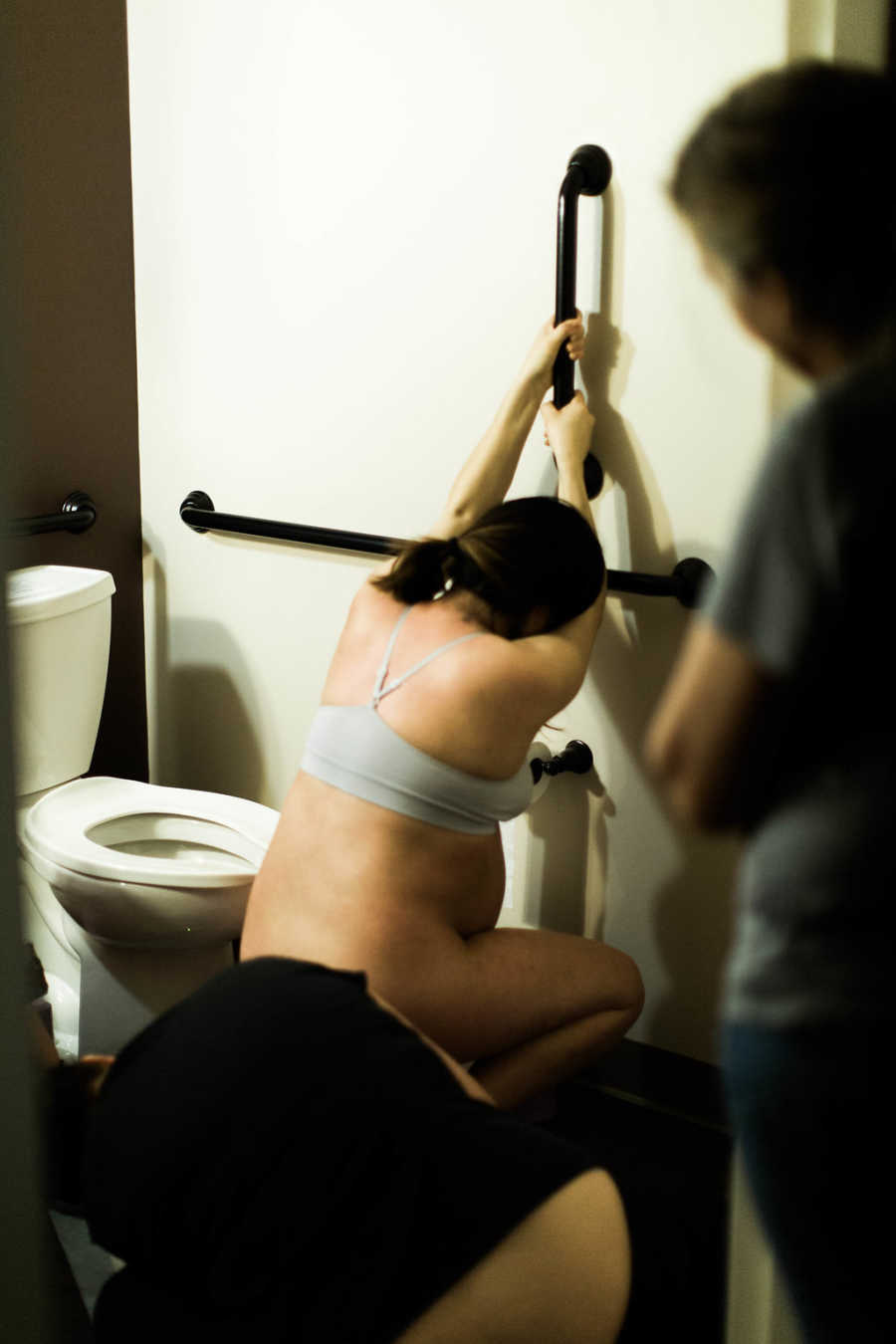 Pregnant woman crouches down holding on to a handle next to toilet