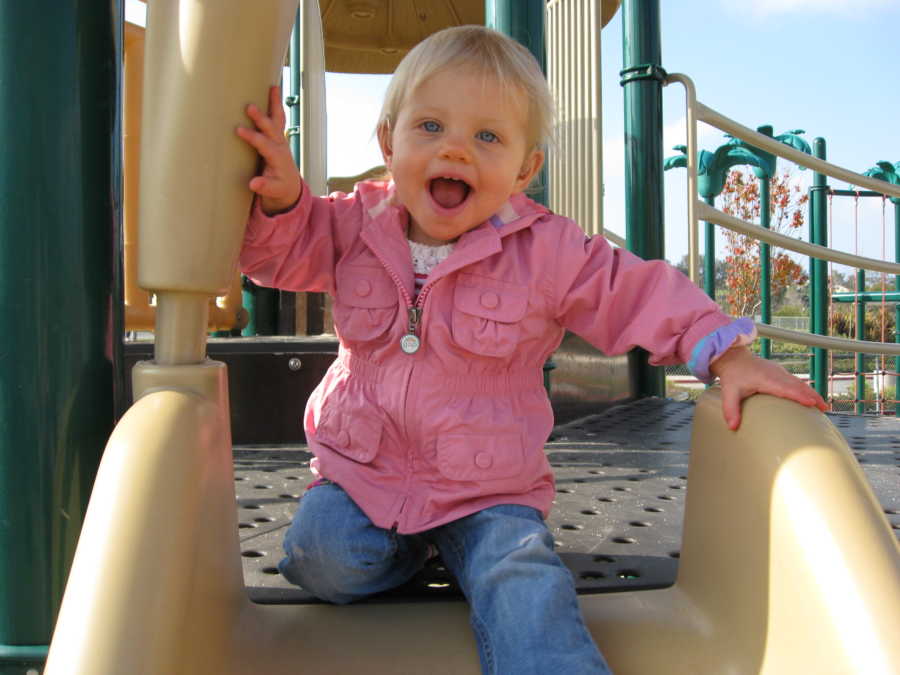 Toddler with special needs smiling as she is about to go down slide