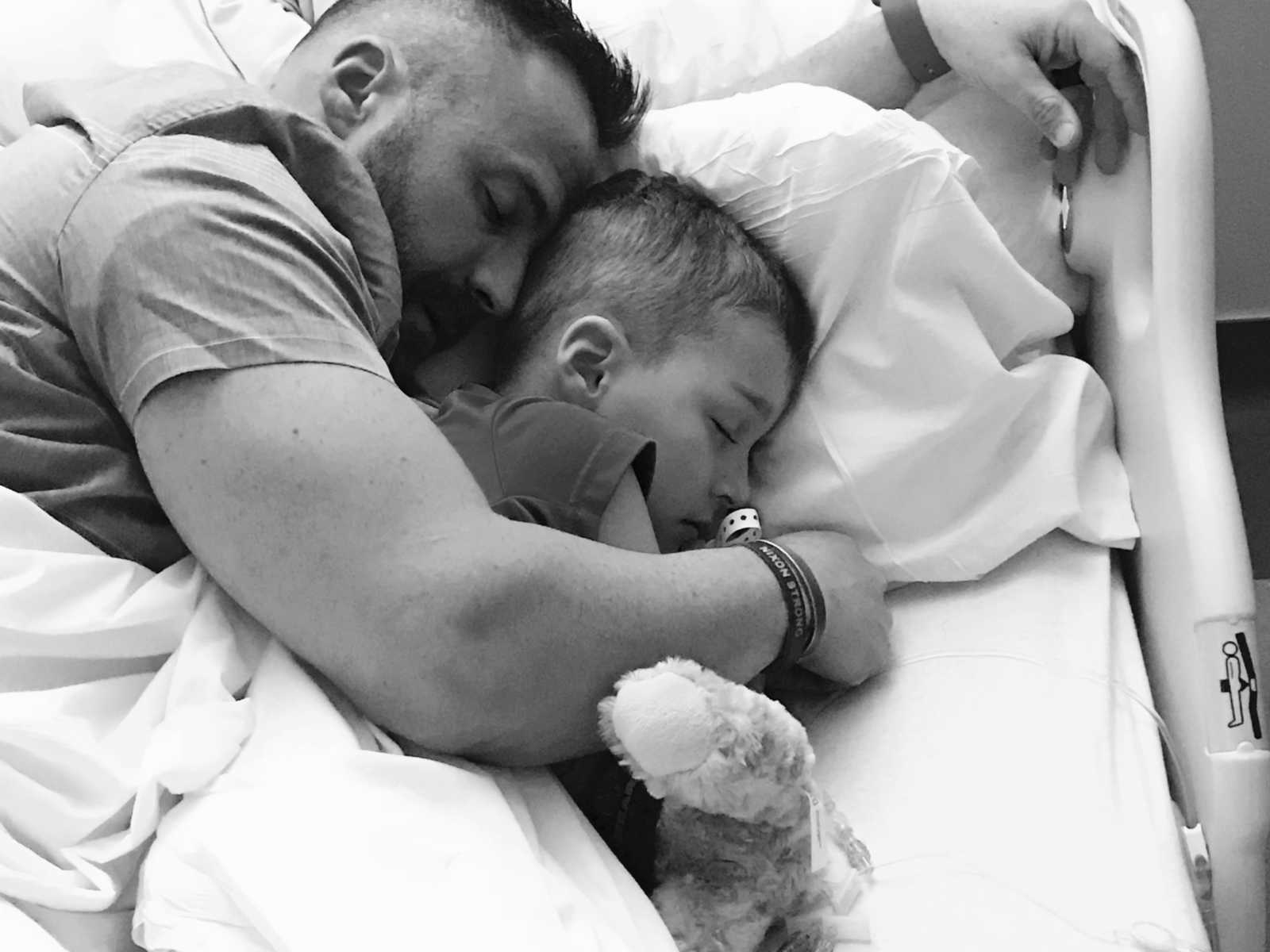 Boy with leg tumors asleep in hospital bed with dad lying next to him