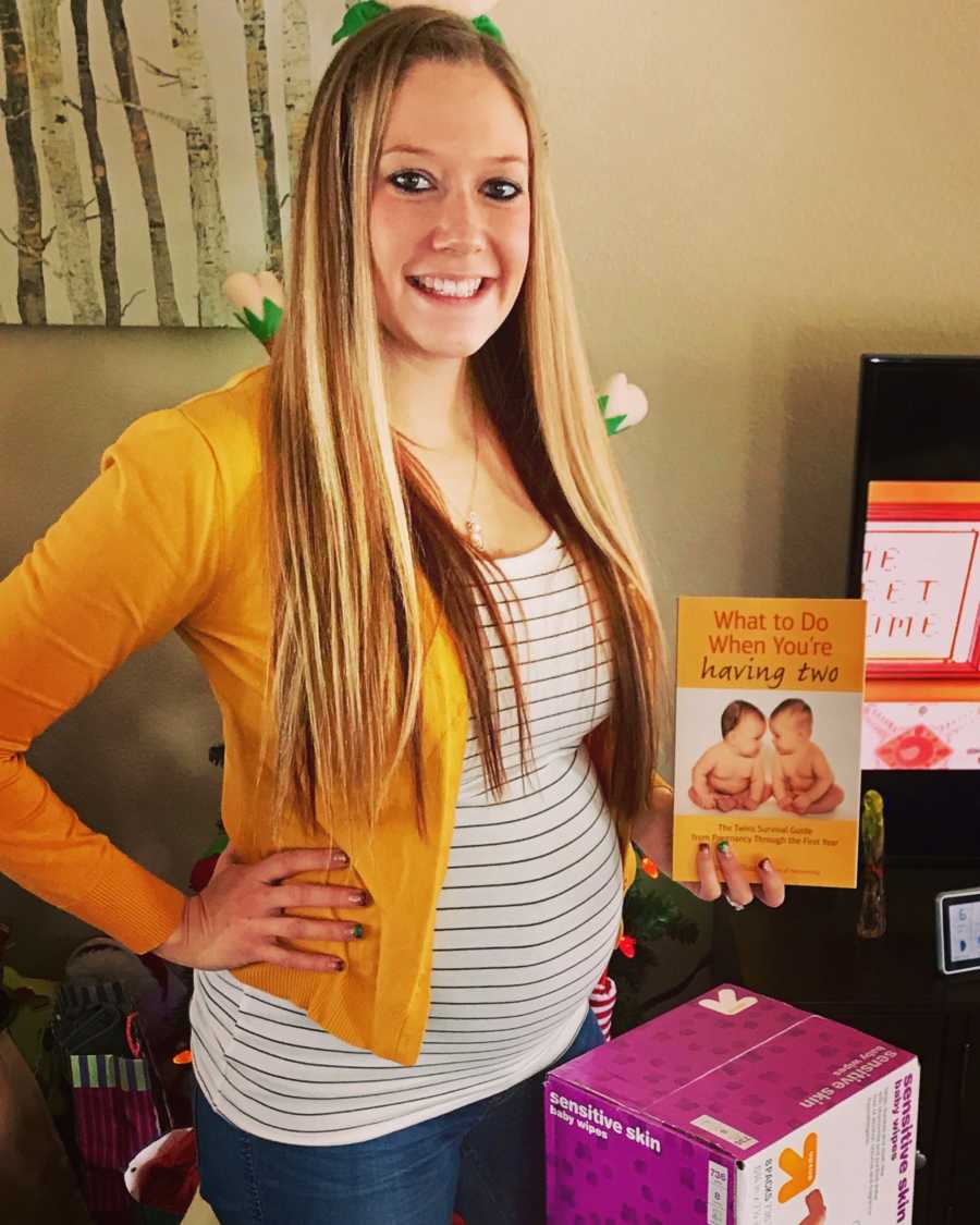 Pregnant woman who had fertility issues smiles while holding up book titled, "What to do when you're having two"