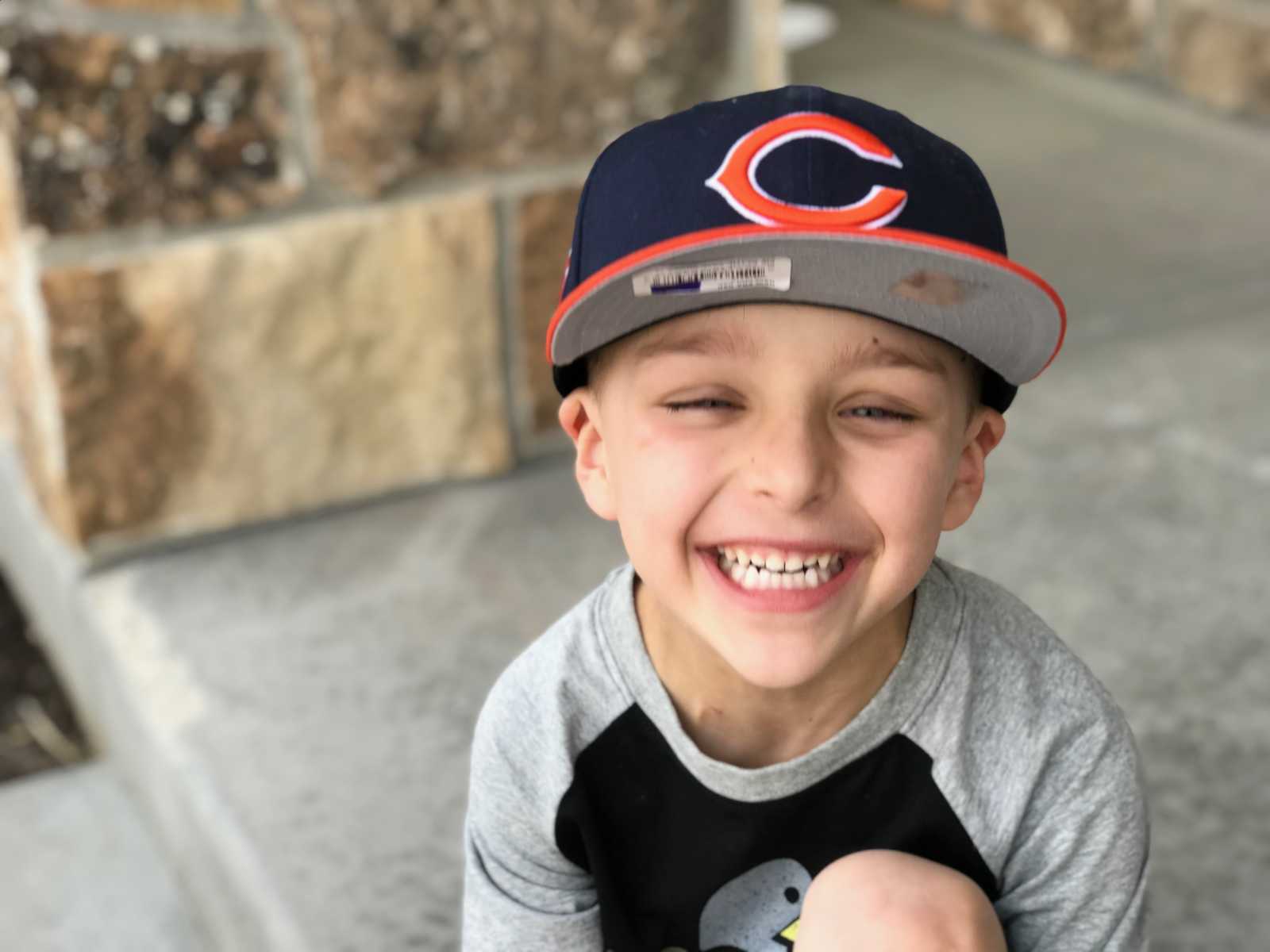 Little boy smiling while sitting in Chicago Bears hat who will have leg tumors later in life