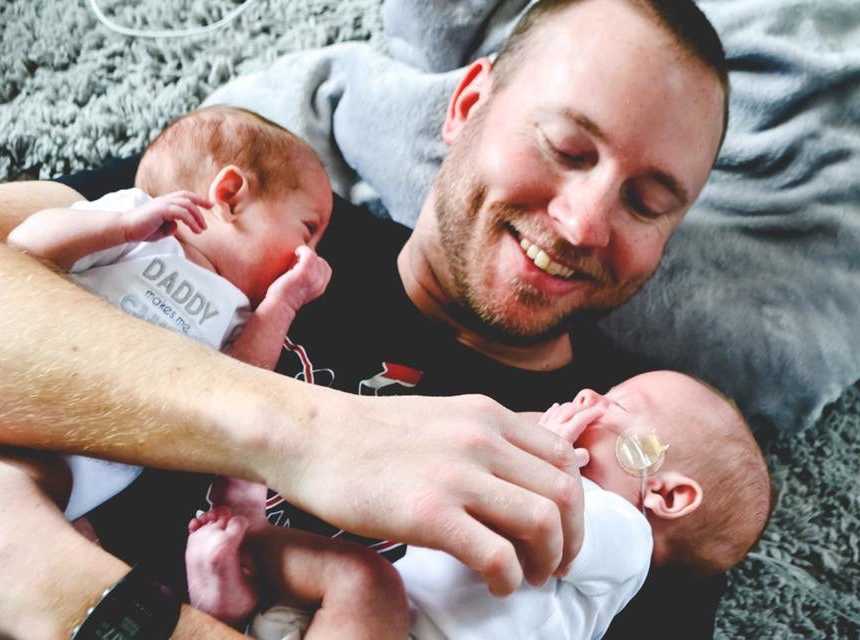 Father whose wife struggled with fertility lies on ground with twin newborns in his arms