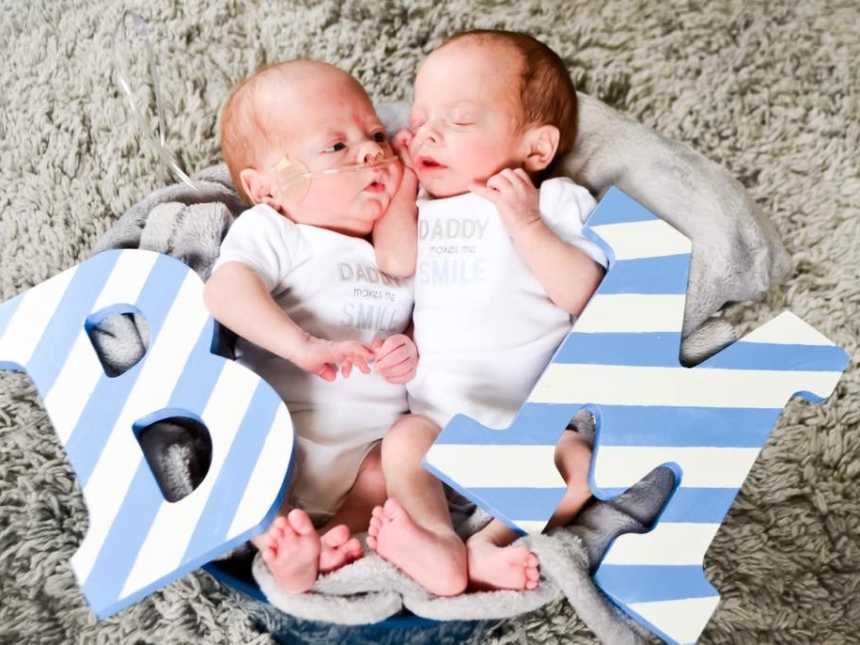 Twin newborns whose mother struggled with fertility lie on ground in blanket with wooden B and M for their names