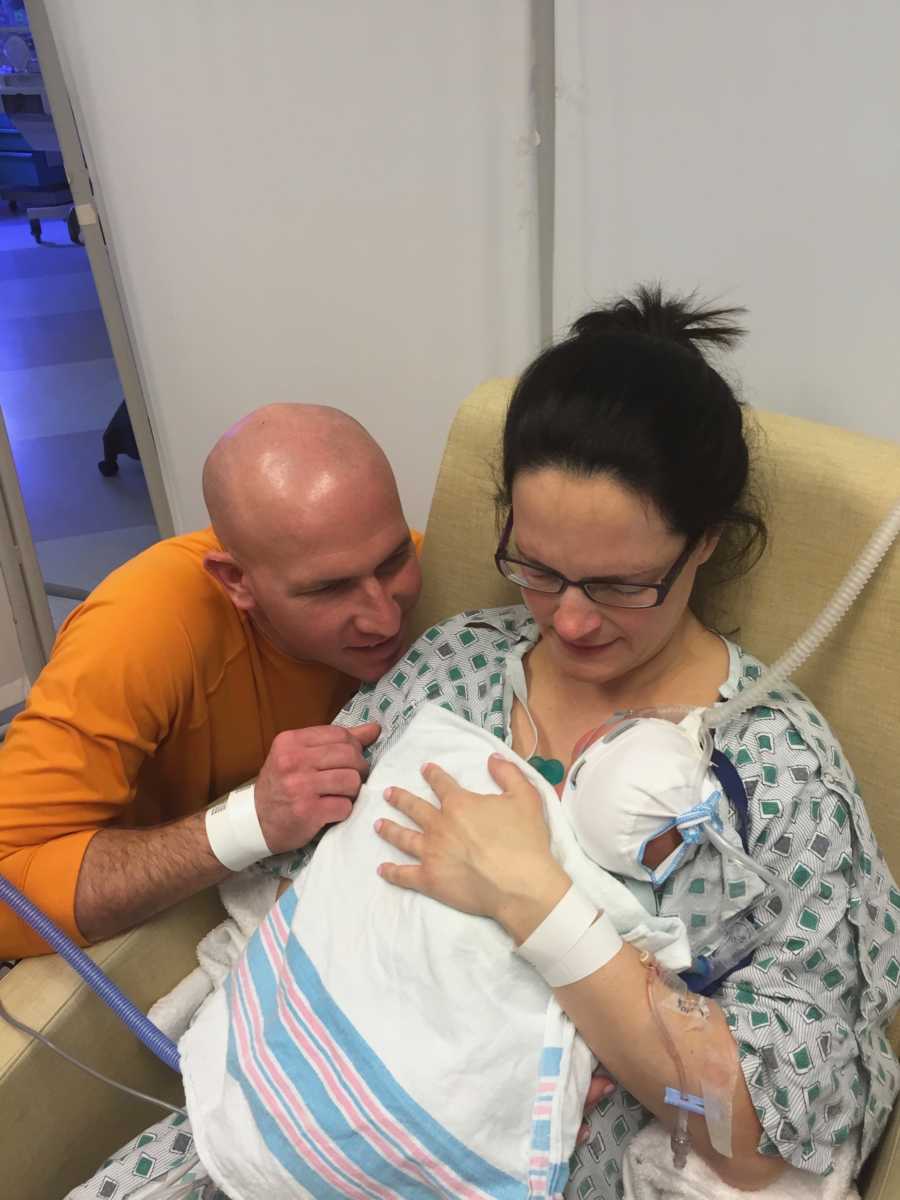 Woman who suffered ruptured appendix holds newborn in hospital with husband crouching next to her