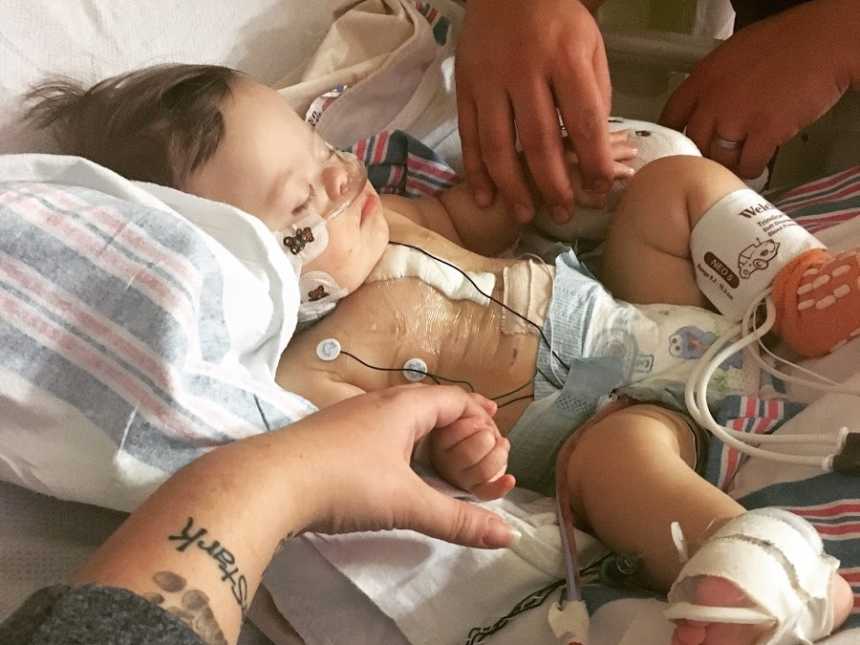 Newborn with down syndrome in NICU holding hands with mother and father