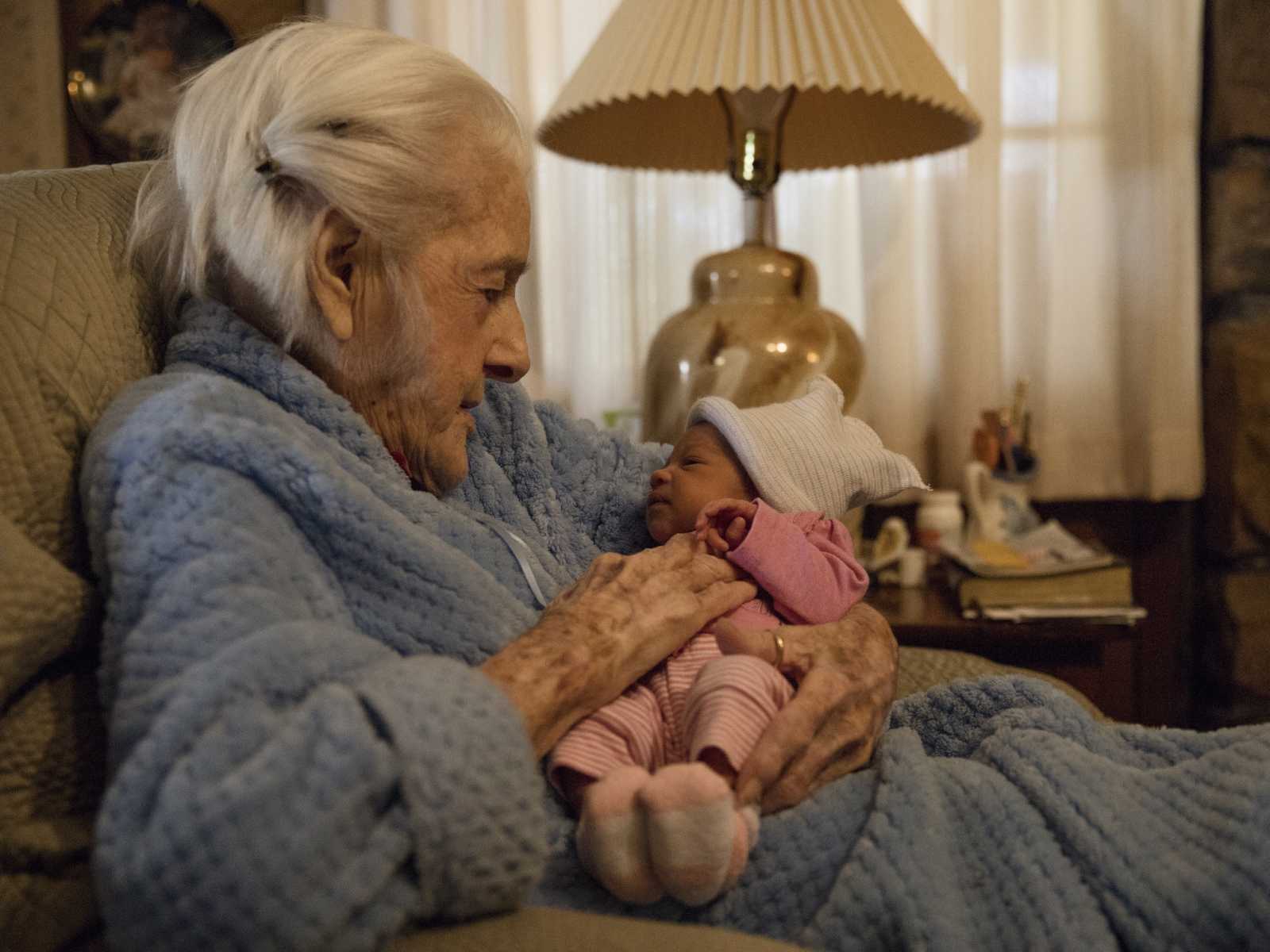 92 year old woman sits looking down at newborn in her lap who is her namesake
