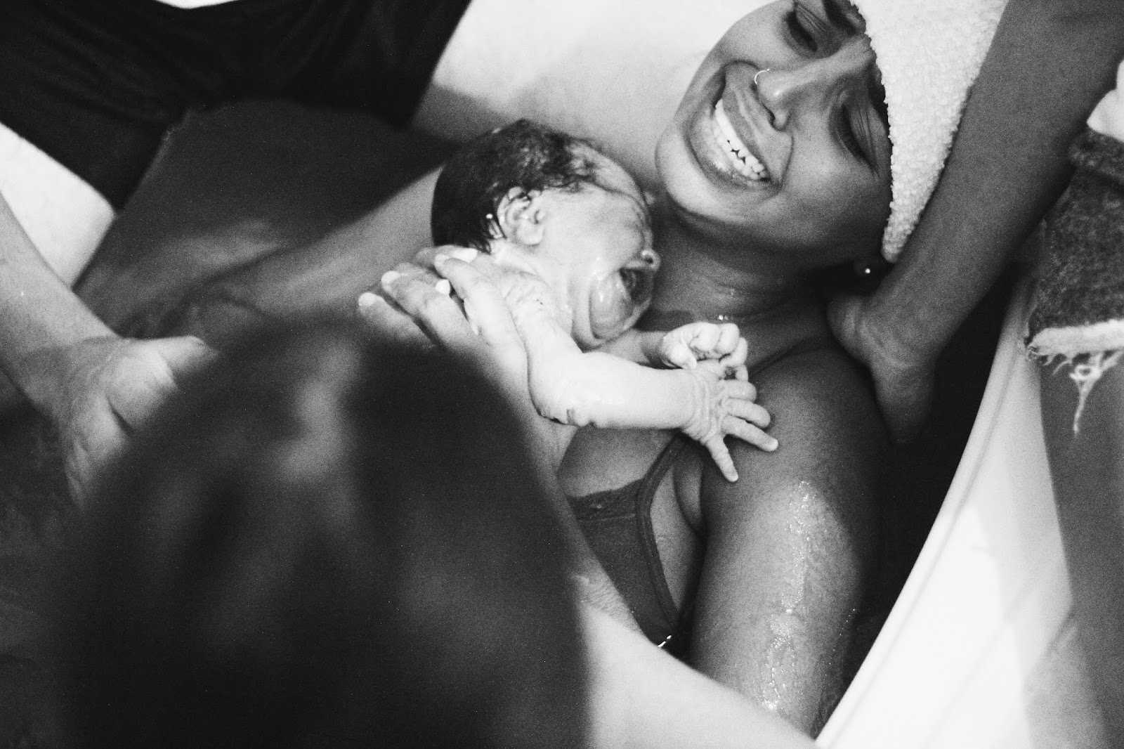 Woman who had water birth smiles as she holds newborn to her chest