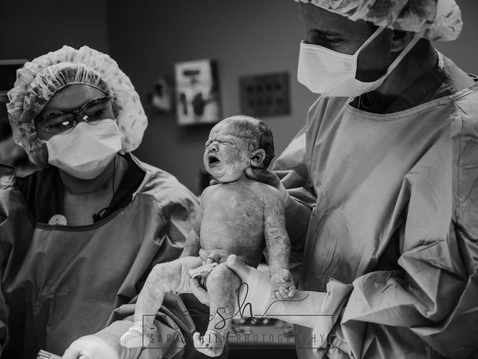 OBGYN holding c-section baby while nurse watches