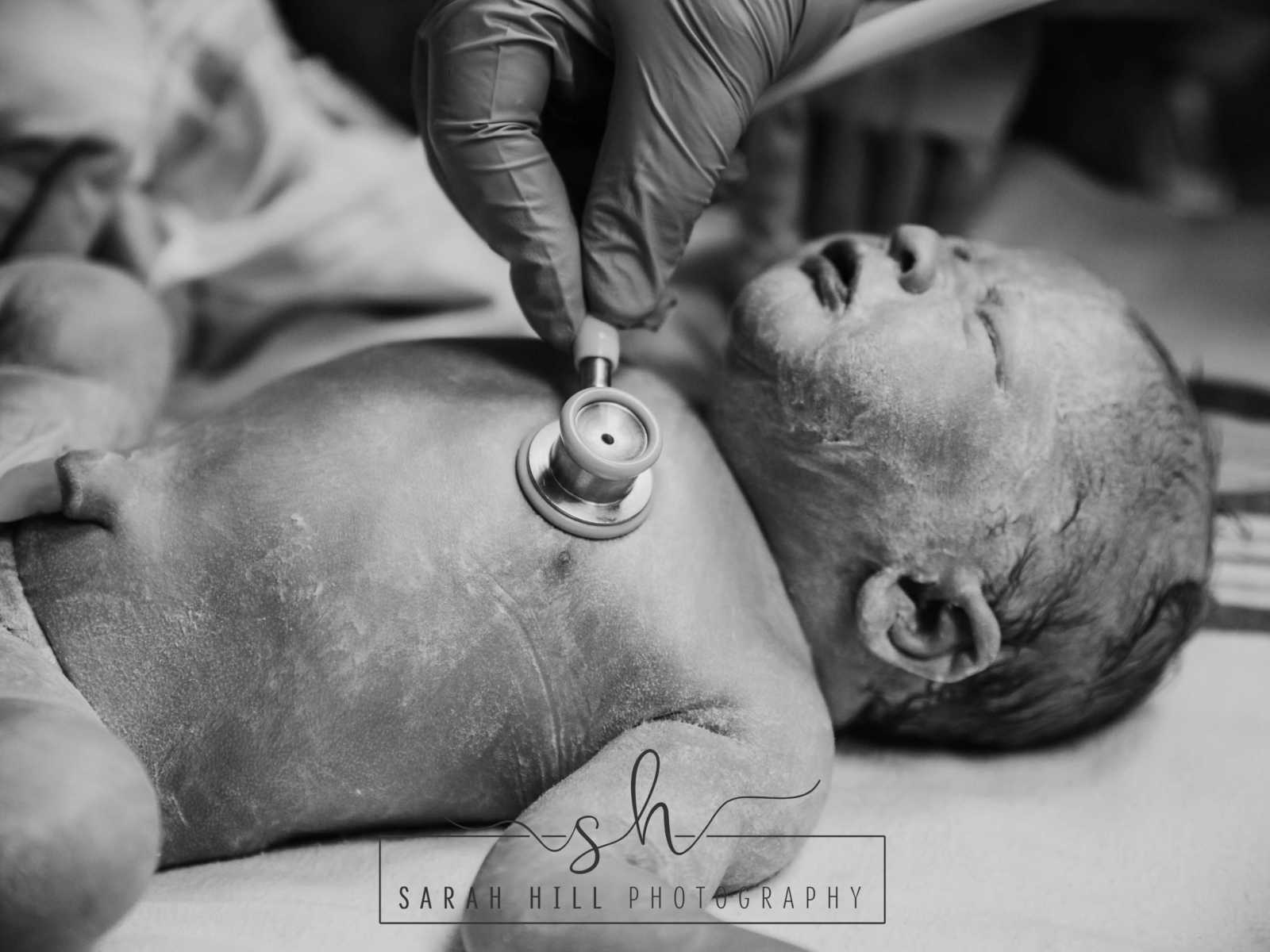 Close up of doctor listening to newborn c-section baby's heart with stethoscope