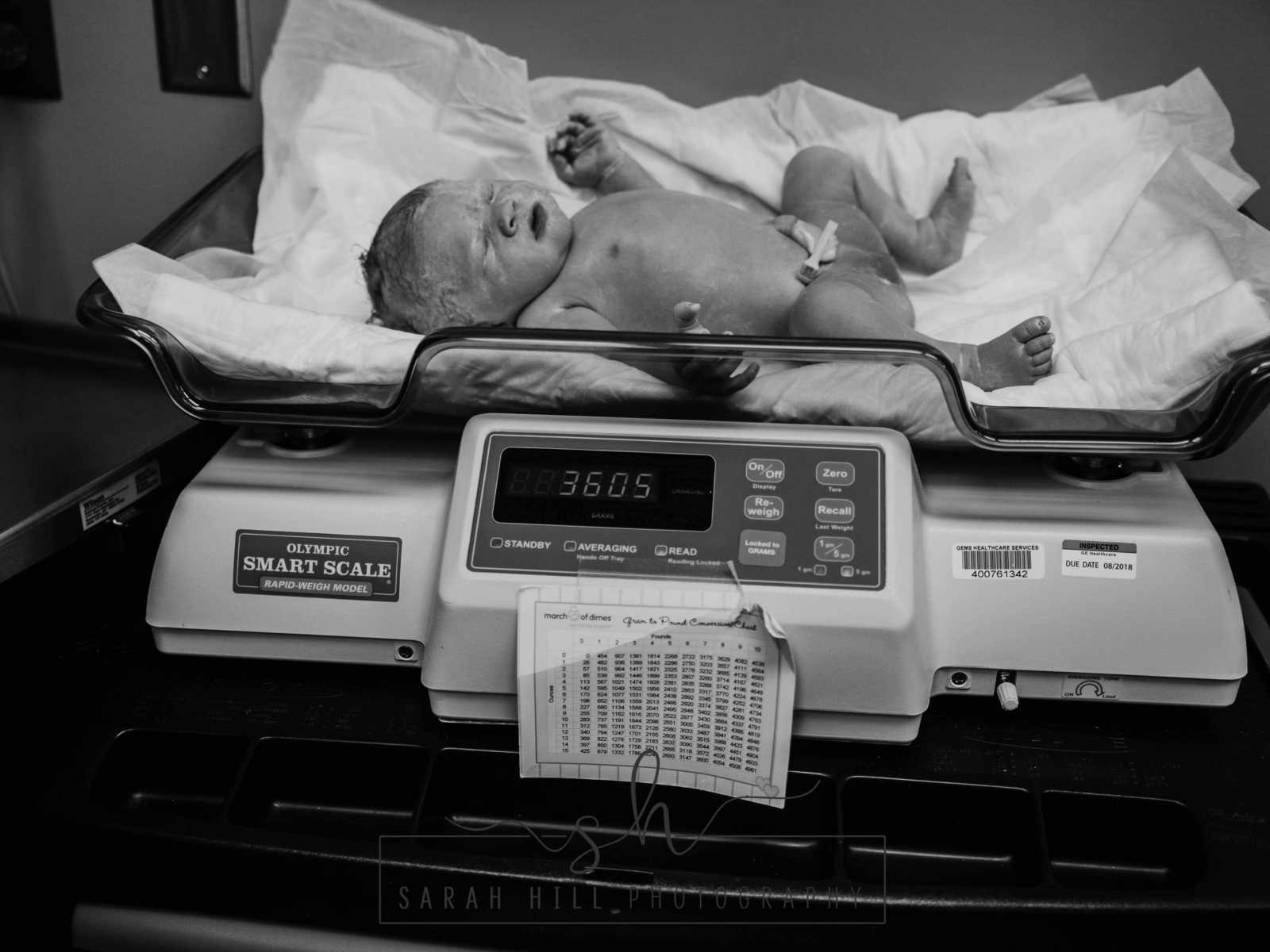 Newborn c-section baby laying on scale 