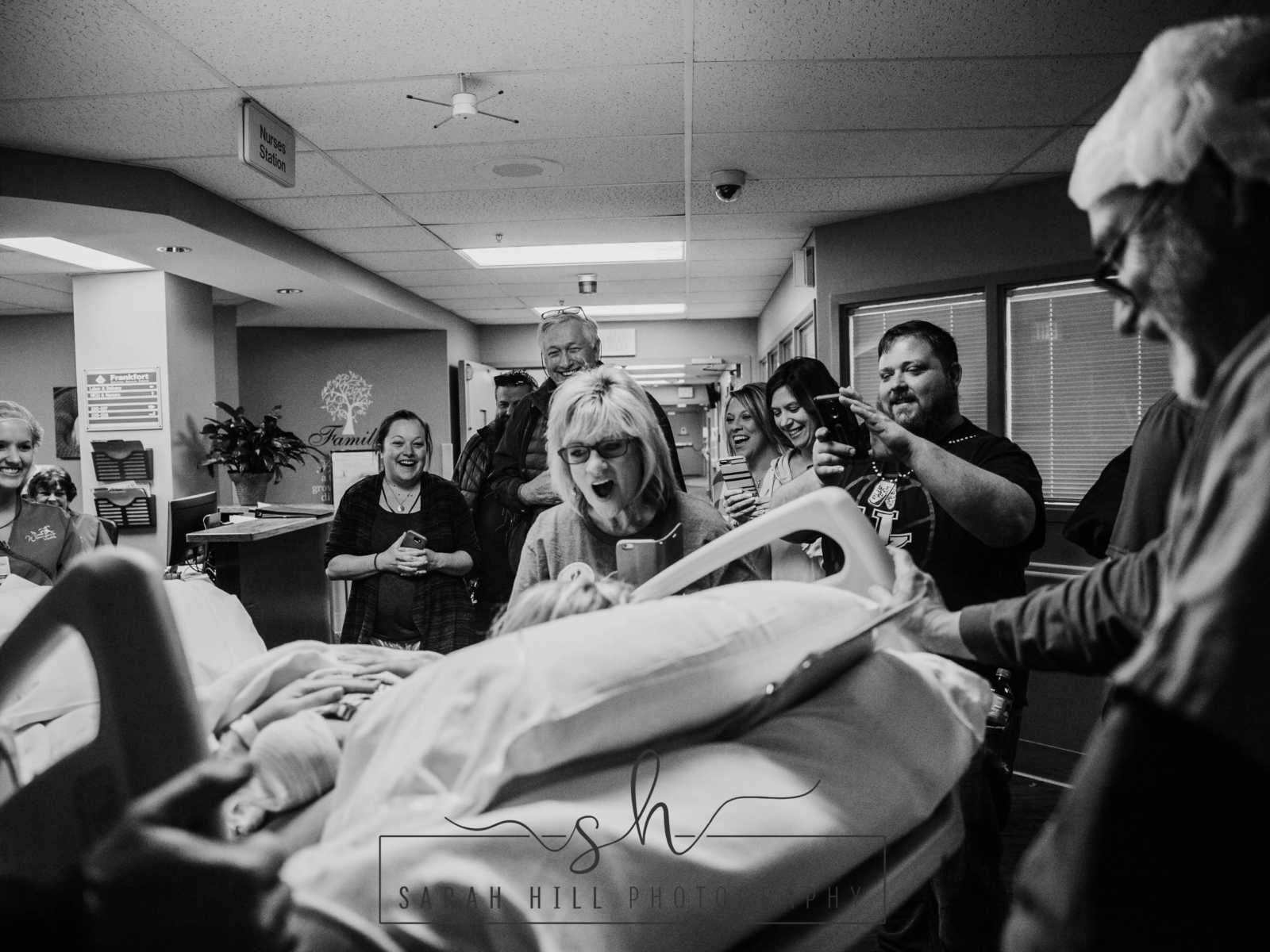 Woman who just had c-section is pushed down hospital hallway with newborn while crowd watches