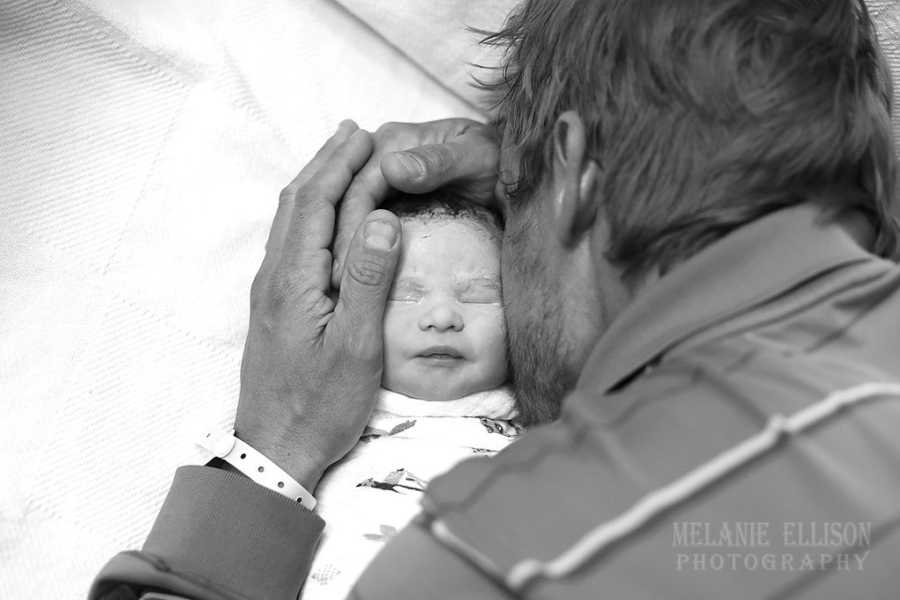 Father holds newborn's head and kisses his cheek