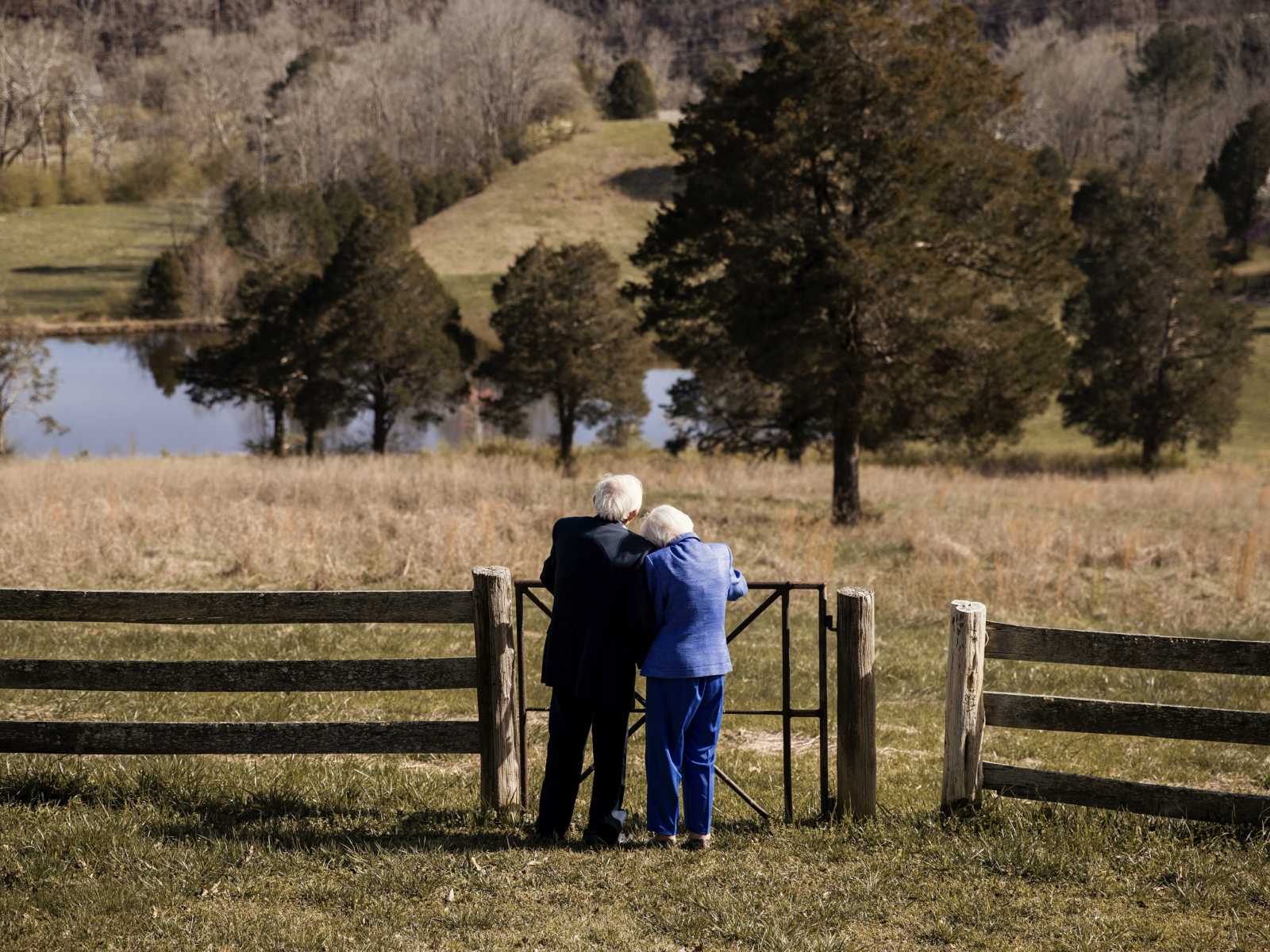 92 year old woman leans on her husband as they stand looking out at grass field 