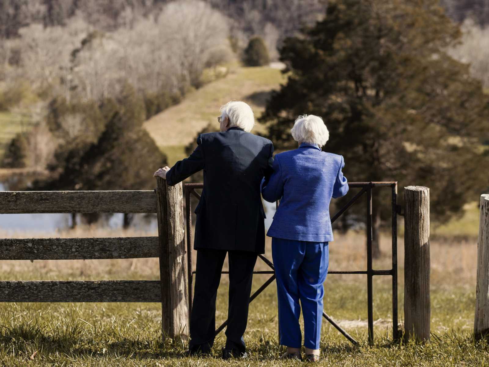 View from the back of 92 year old woman standing with her husband by a fence in their yard