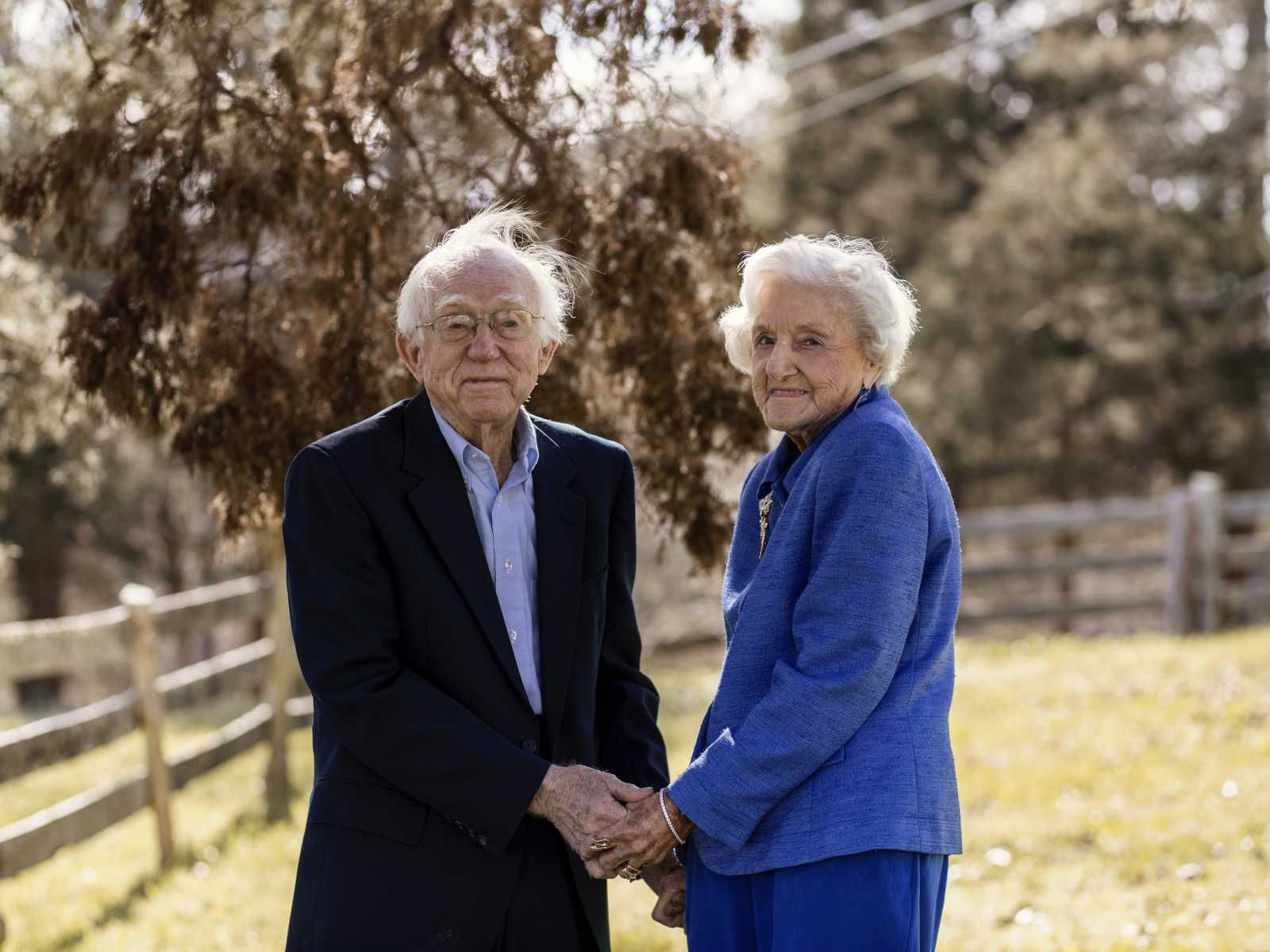 92 year old woman holds hand with her husband in their yard