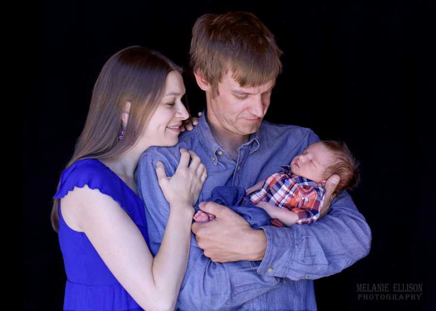 Mother and father look at newborn baby who father is holding in his arms